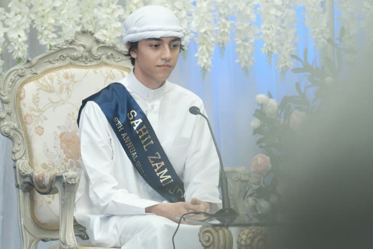 Student seated on stage at an Abu Huraira Center Quran competition