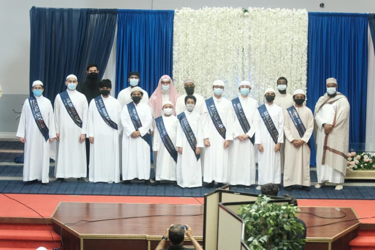 Group photo of Quran competition participants wearing sashes on stage