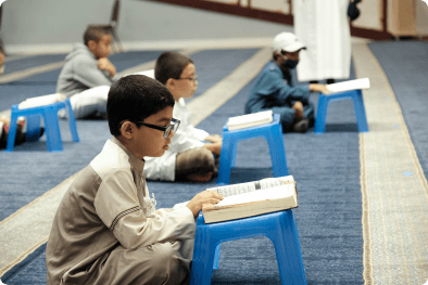 Boys reading the Quran on small blue desks
